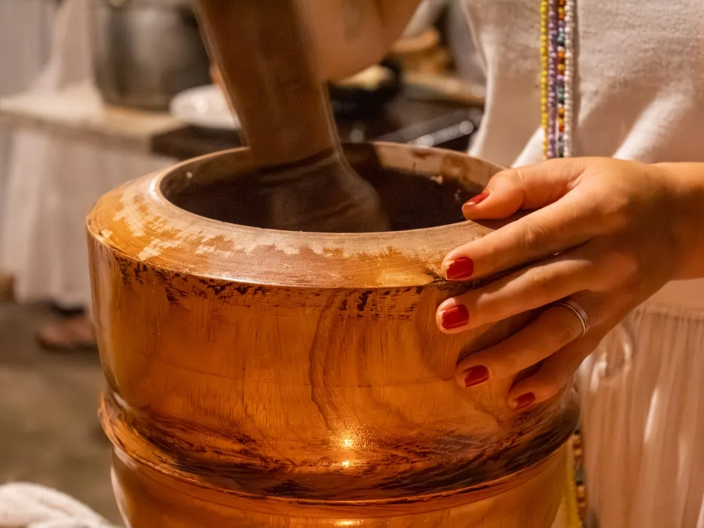 Mãos preparando o axé no pilão de madeira, na tradição da Jacutá